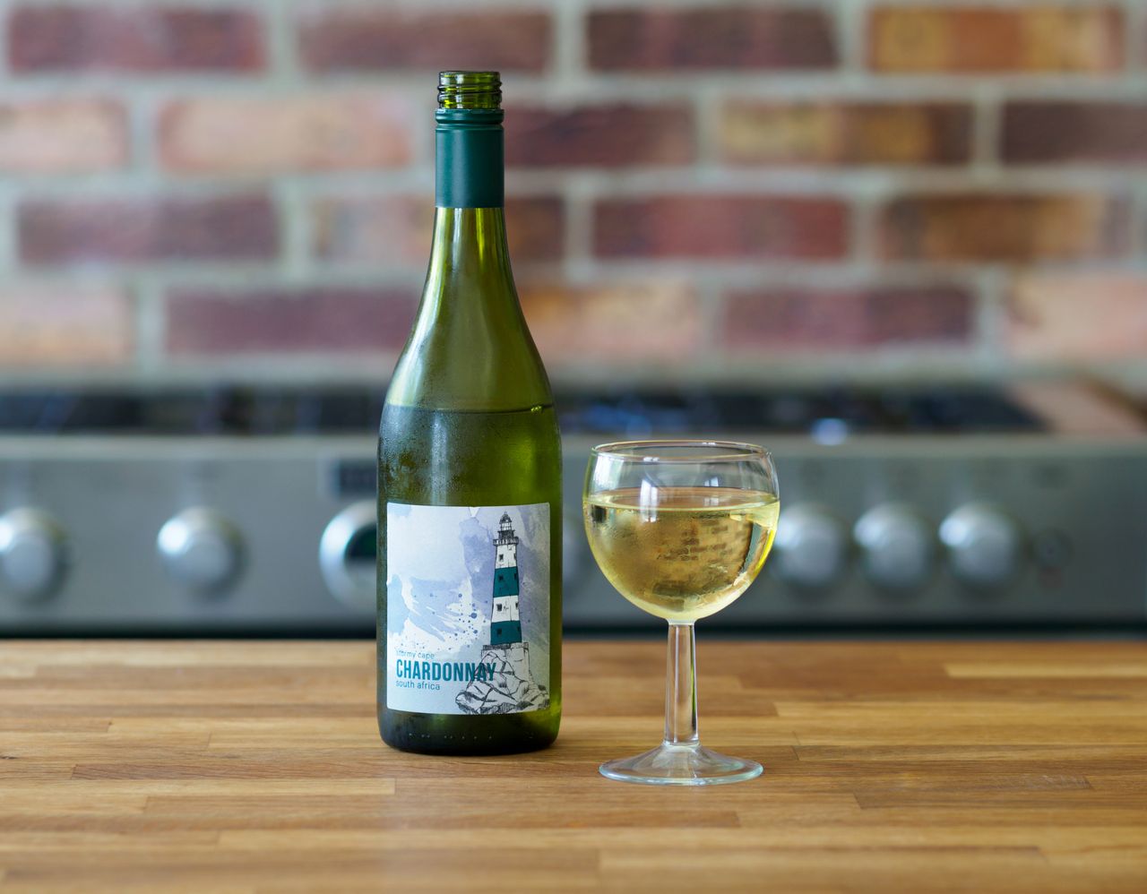 Close-up of a Chardonnay wine bottle and glass on a wooden table with a brick background.